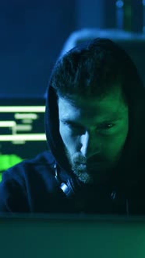 Ein Mann in einem Hoodie starrt in einem dunklen Raum aufmerksam auf seinen Laptop