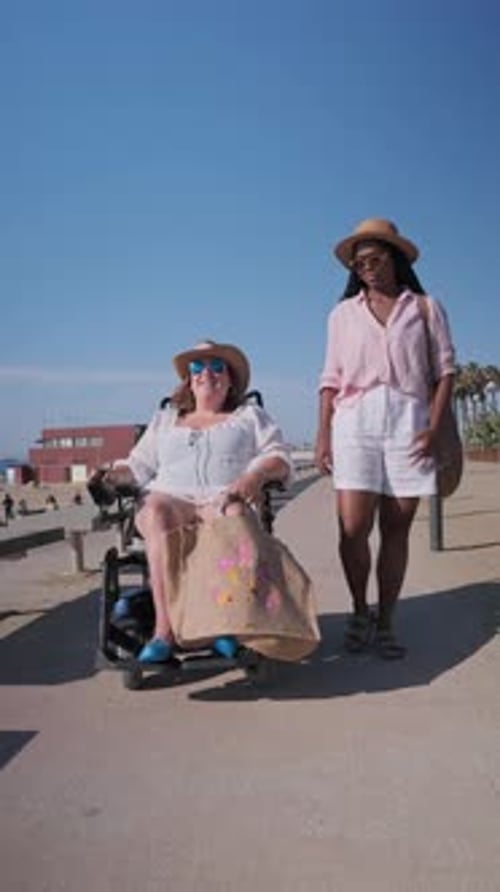 Woman Pushing Friend in Wheelchair on Beach Boardwalk in Slow Motion