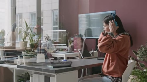 Asian Female Software Developer Enjoying Music while Working on Laptop