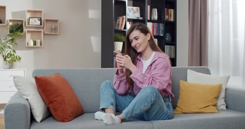 Woman Using Cell Phone Smiling on Sofa at Home