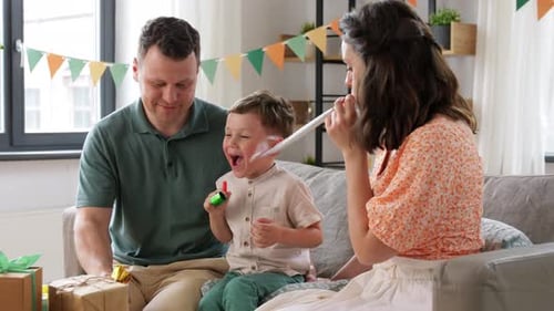 Family celebrates birthday together at home blowing noisemakers