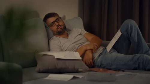 Man Sleeping on Couch Surrounded by Bills