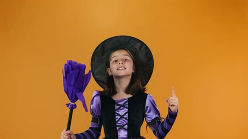 Girl Dressed as Witch Holds Broom and Points Up
