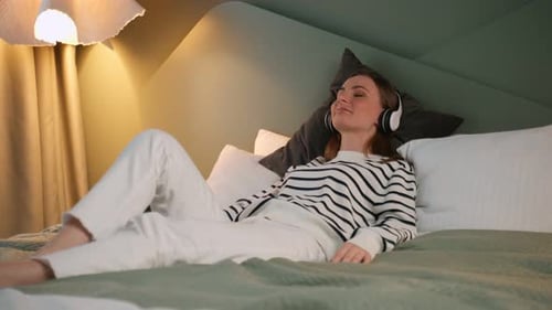 Woman Relaxing on Bed Listening Music with Headphones