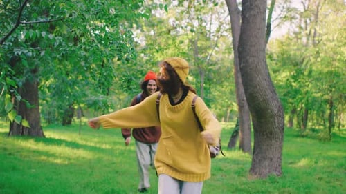 A Couple Runs in the Park Laughing and Playing Among the Trees The Man Chases the Woman Both