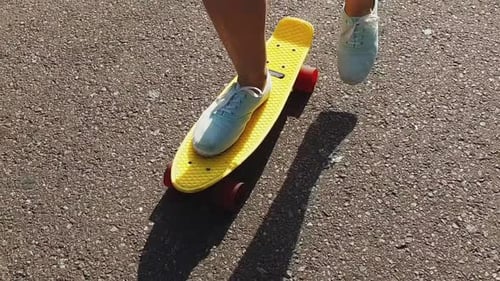 Teenage girl feet riding modern cruiser skateboard on road in slow motion