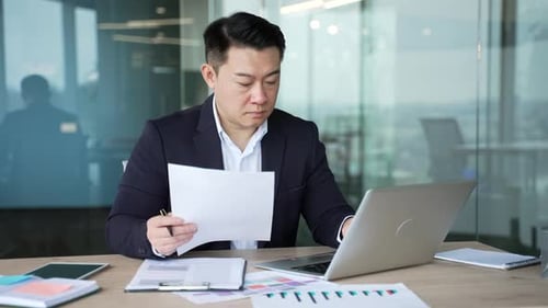Busy serious asian businessman in a formal suit analyzing financial documents checking data