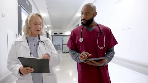 Diverse male and female doctors in discussion using tablet in hospital corridor, slow motion