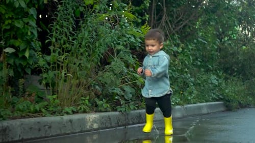 A Child Joyfully Playing in the Rain While Wearing Bright Yellow Boots in Nature