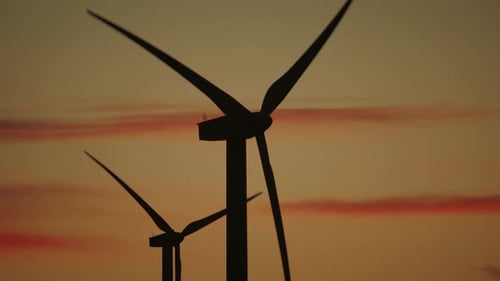 Große Windturbinen mit großen Rotorblättern erzeugen grüne Energie bei wunderschönem orangefarbenem Sonnenuntergang.