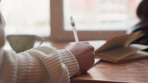 Close Up Hand Writing From Novel with Natural Window Light on Wooden Table