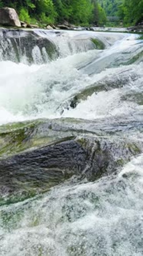 Stormy streams of water and waterfalls of a mountain river. Vertical video.