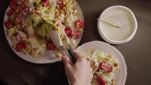 Der Koch legt mit einer Zange etwas Caesar-Salat auf den Teller. Er besteht aus Käsecroutons und Salatblättern