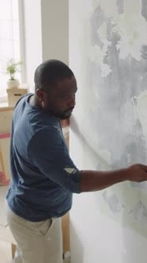 African American Man Scraping off Old Paint from Wall Carrying out Renovation