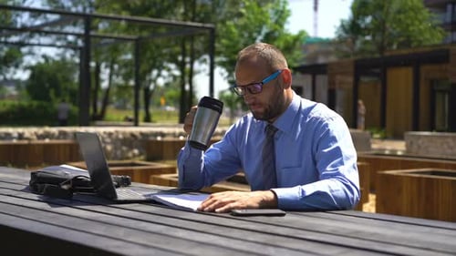 Junger Geschäftsmann liest Magazin und trinkt Kaffee im Park der 30er Jahre