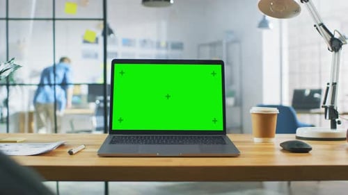 Laptop on the Desk in the Office Shows Green Mock-up Screen. In the Background Bright Creative Open