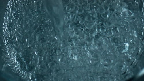 Sprudelndes Wasser füllt das Glas von oben, Luftblasen steigen auf, explodierende Oberfläche
