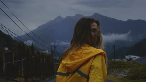 Happy Woman Walks Toward Mountains in Yellow Raincoat