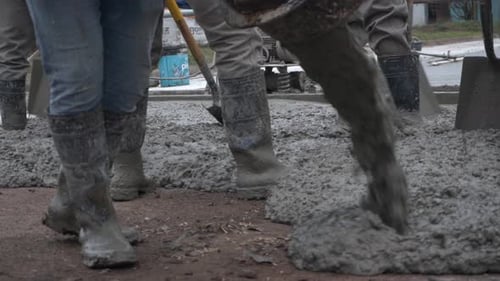 Beton wird gegossen, während Arbeiter mit Schaufeln eine Straße pflastern.