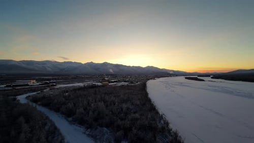 Sunrise over the frozen river in a quiet village surrounded by mountains in winter