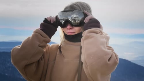 A Beautiful Girl Puts on Winter Goggles or a Mask for Snowboarding Big Blue Eyes Hair Moving in the