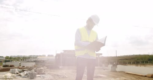 Male Engineer in Uniform and White Helmet Makes Notes in Notebook at Work
