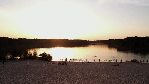 Fotografando de um quadricóptero de praia no lago cercado por árvores ao pôr do sol e pessoas que estão
