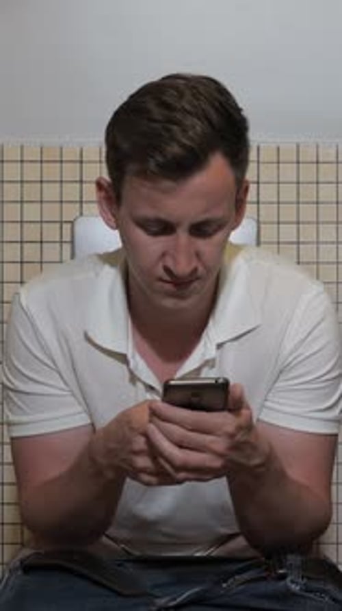 Man Pushing Hard While Using Smartphone on Toilet