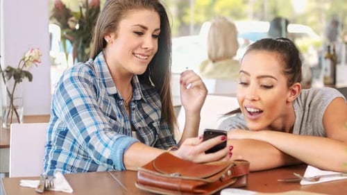 Young latina woman reacts happily to a photo on her smart phone at local restaurant