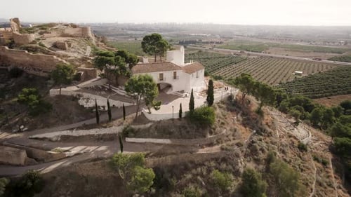 Drone flyby top view over a white Hermitage and castle ruins among trees on top of the hill