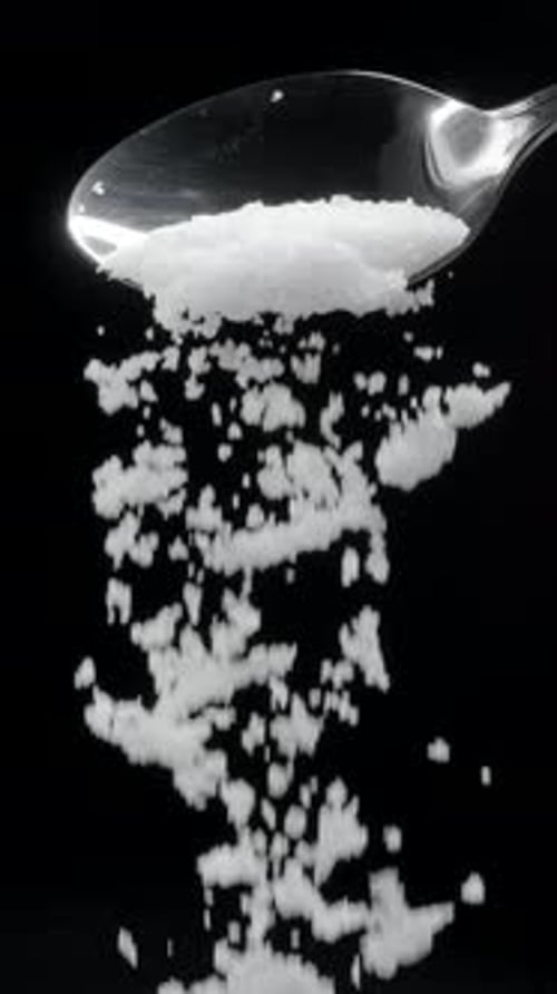 Adding salt or sprinkling salt on black close up.