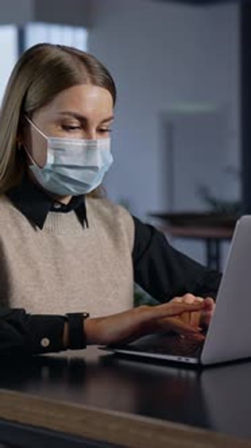 Woman Works on Laptop Wearing a Mask