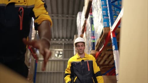 Two warehouse workers are lifting boxes of merchandise on a pallet jack to store on a shelf