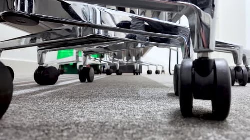 Caster wheels underside office chairs moving across carpet. Low angle, push forward