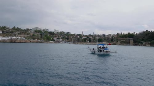Fliegen Sie um ein Boot herum, das entlang der Küste in Stadtgebäuden im Stadtbezirk im Hintergrund fährt Antalya