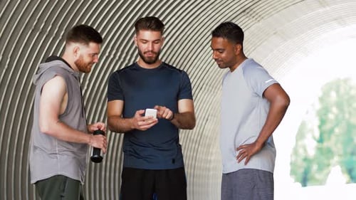 Three men looking at phone in tunnel
