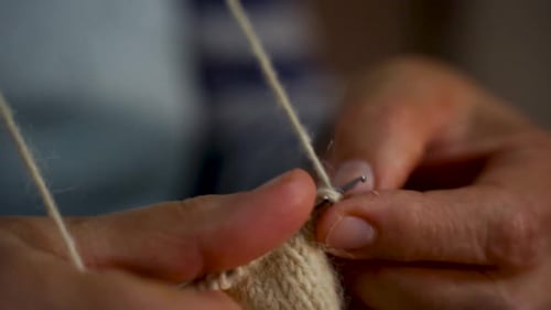 Hands of old woman knitting handmade wool socks with needles at home, slow motion, close up grandma