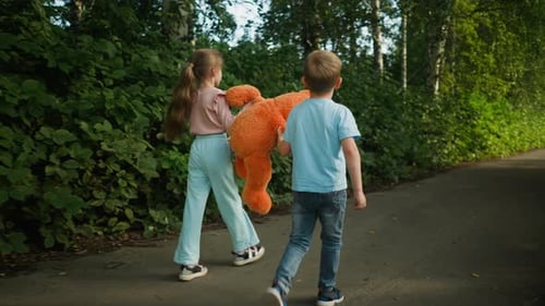 Rear View of Siblings Walking on Path with Lifted Teddy Bear in Hand