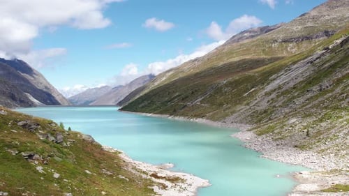 aerial flight over turquoise blue lake in the swiss alps during beautiful summer months, hiking para