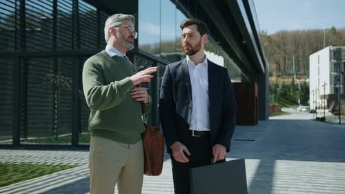 Two men in suits converse outside office building
