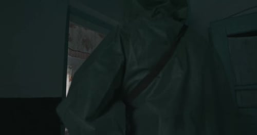 Man in a Vintage WWII Gas Mask and Hazmat Suit Entering a Cottage Carefully Looking Around Behind