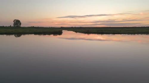 Dolly, Aerial shot over a green field with a lake at sunset.