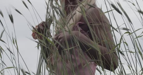 Young Black Girl With Long Blonde Hair In Pink Silk Gown Standing In Field of Tall Grass. Close Up.