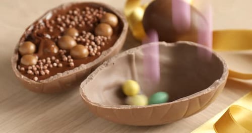 Candies falling into chocolate Easter egg on wooden table, closeup