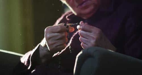 Die Hand einer älteren Frau spricht ein Gebet, indem sie in der Tradition seiner Religion einen Rosenkranz berührt