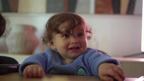 Smiling toddler in blue outfit sitting at dining table with playful expression during family