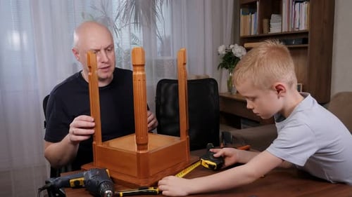 A Little Boy and His Father are Repairing a Chair at Home Using Various Tools