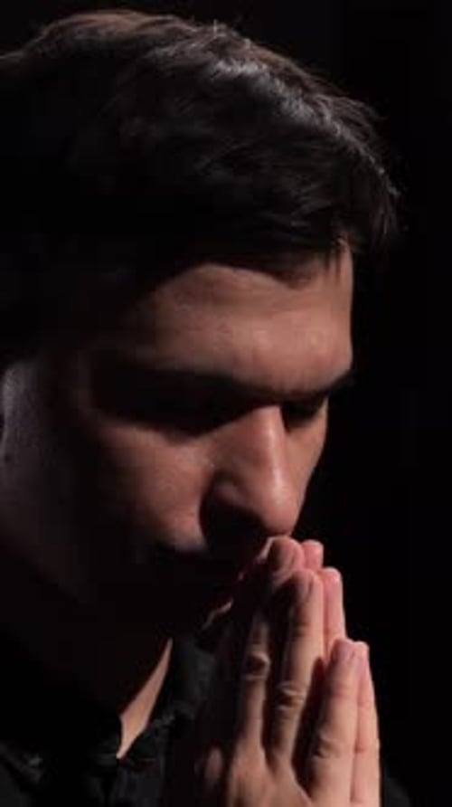 Man Clasping Hands in Prayer with Dark Background