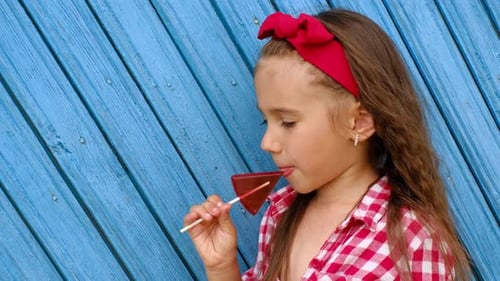 Girl Enjoys Red Lollipop by Blue Wood Wall