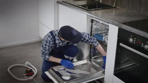 Professioneller Arbeiter in Overalls repariert einen Geschirrspüler in einer Wohnung